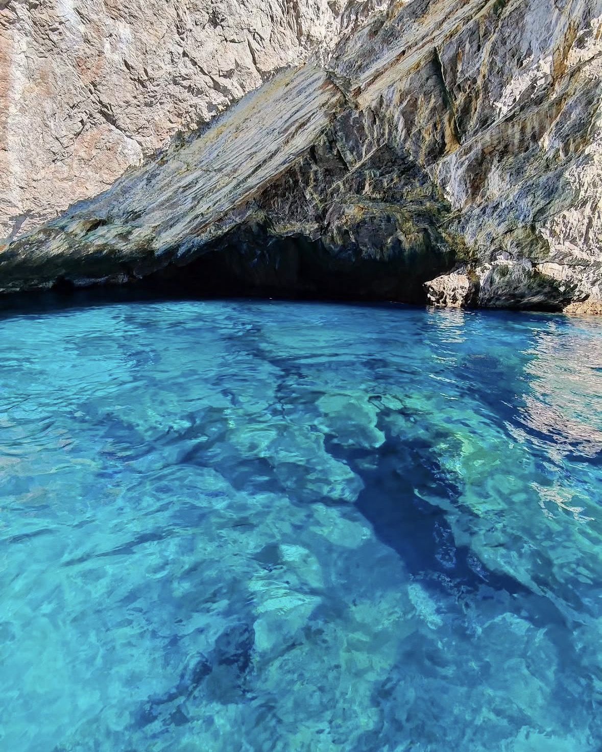 Tourists aboard a small wooden dinghy entering the glowing interior of a Croatian sea cave